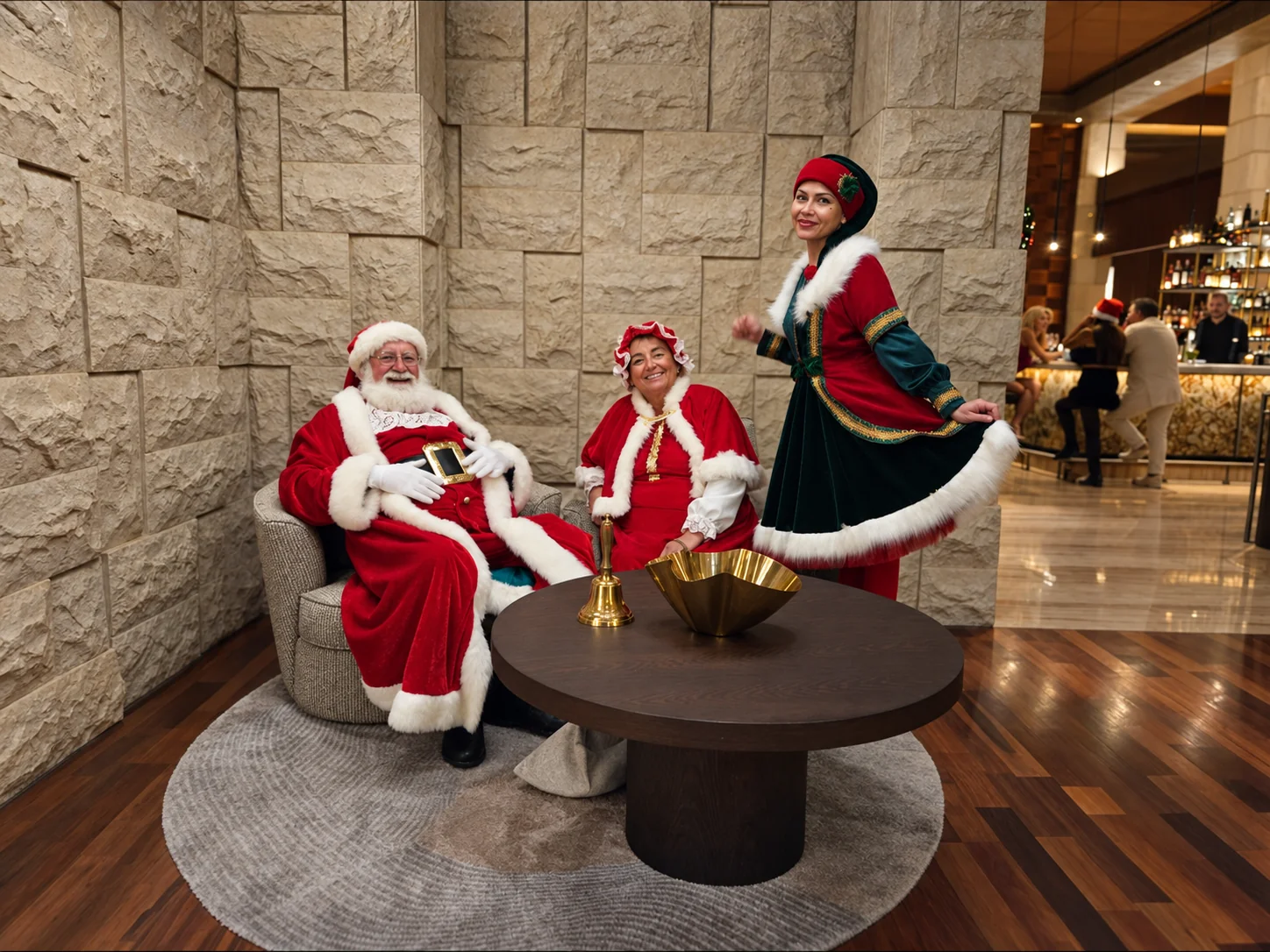 Santa, Mrs Claus and an elf beside a stone wall with a golden bell