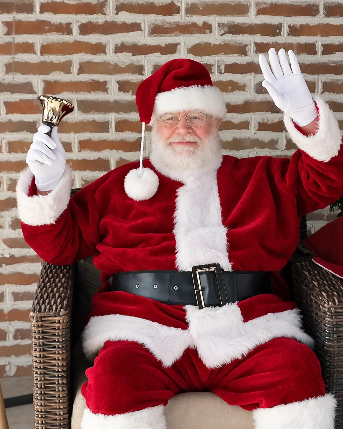 Santa ringing a bell and waving against a rustic brick wall